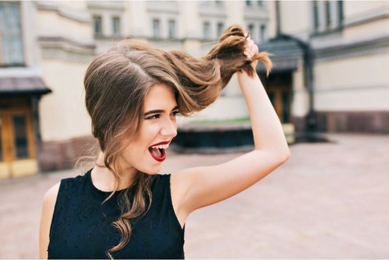 Vrouw met bruin haar en rode lippen, trekt aan haar lokken.