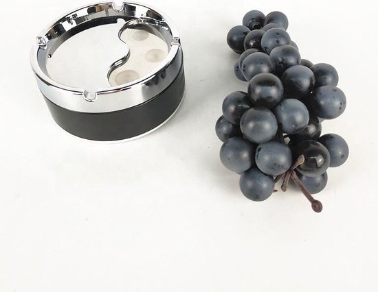 Zwarte draaiasbak met yin-yang motief en chroomkleurige rand, naast een tros donkerblauwe druiven.