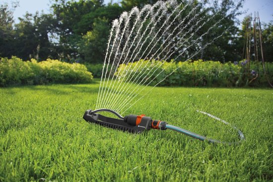 GARDENA zwenksproeier met oranje en zwarte accenten sproeit water over een groen gazon.