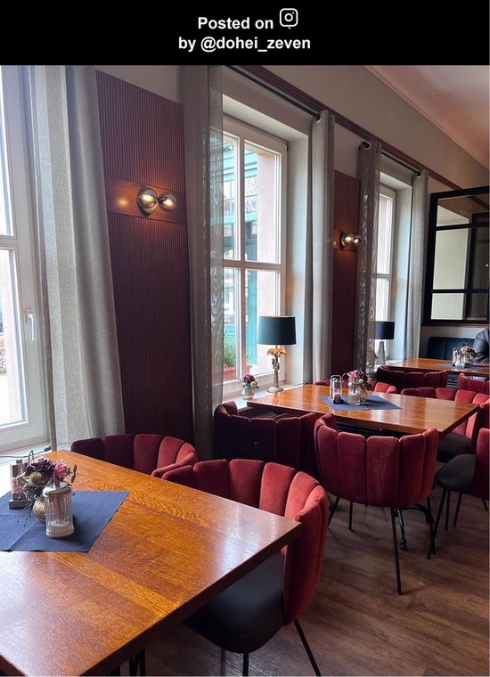 Gezellige zithoek in restaurant met houten tafels, rode fluwelen stoelen en tafellampen met zwarte kappen.