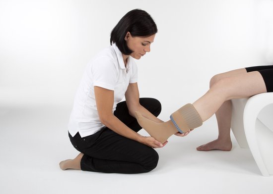 Vrouw helpt man met het aantrekken van steunkousen met een beige, geribbelde tool.