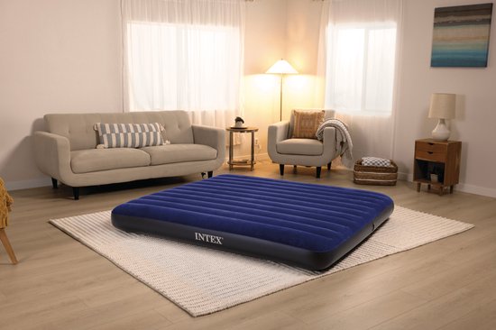 Een donkerblauw Intex luchtbed met ribbels ligt op een wit tapijt in een woonkamer.