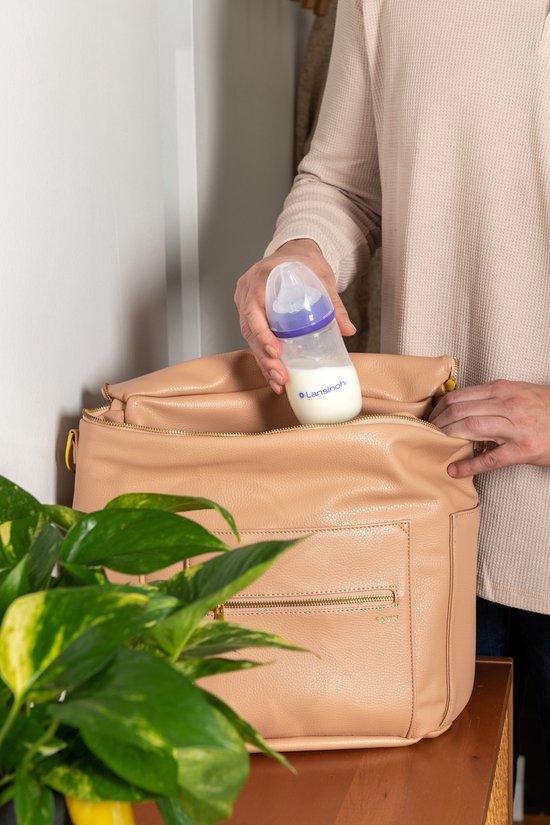 Een hand legt een Lansinoh babyfles met melk in een bruine tas. De fles heeft een paarse ring en Natural Wave speen.
