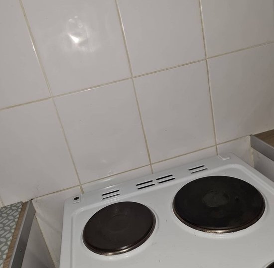 Witte keuken- en wandtegels met grijze voegen boven een wit fornuis.