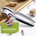 Zilverkleurige knoflookpers met zwarte handgrepen, liggend op een lichte achtergrond met knoflook.