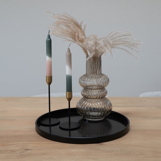 Zwart rond dienblad met twee kaarsen, een glazen vaas met siergrassen op een houten tafel.