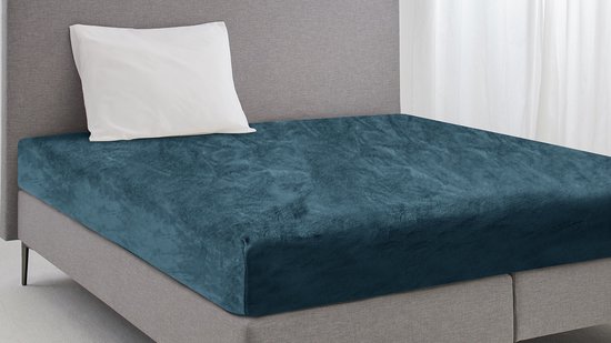 Donkerblauw flanellen hoeslaken op een bed met grijs hoofdbord en wit kussen.