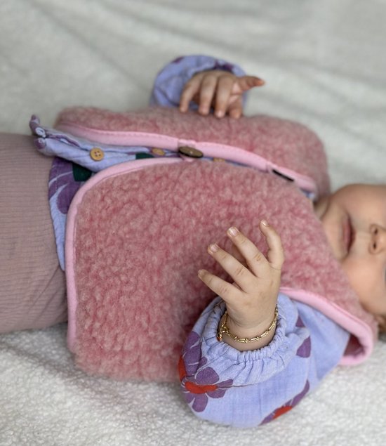 Baby in roze wollen gilet en paars bloemenprint shirtje.