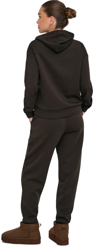 Vrouw met de rug naar de camera, draagt een donkere joggingbroek en hoodie.