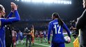 Vrouwelijke voetballer met nummer 12 op blauw shirt, bal in hand, kijkt naar tegenstanders.