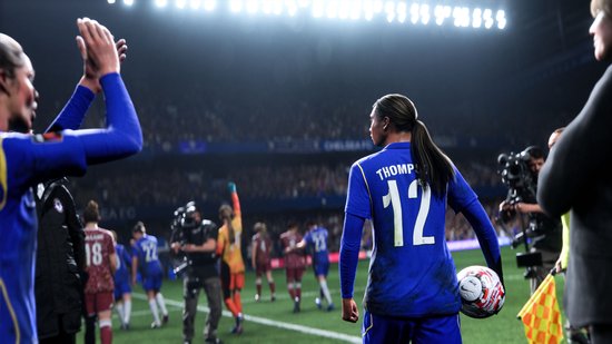 Vrouwelijke voetballer met nummer 12 op blauw shirt, bal in hand, kijkt naar tegenstanders.