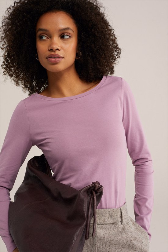 Model met een lila longsleeve en een gemêleerde grijze broek, met donkerbruine tas.