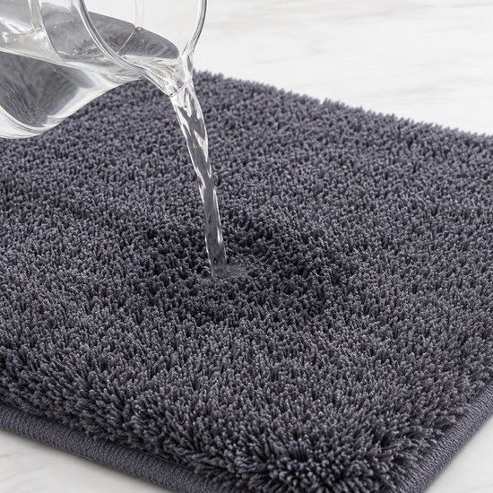 Water dat op een donkergrijze, pluizige badmat wordt gegoten, toont de absorberende textuur.