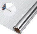 Rol zilverkleurige zelfklevende folie met ruitjespatroon, schaar knipt de folie.