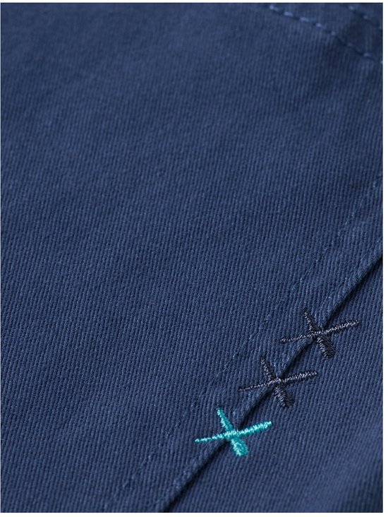 Detail van donkerblauwe stretch katoenen chino broek met turkoois en zwarte kruissteek details.