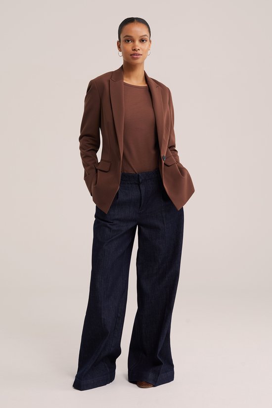 Model draagt een bruin T-shirt, bruine blazer en donkere wijde broek.