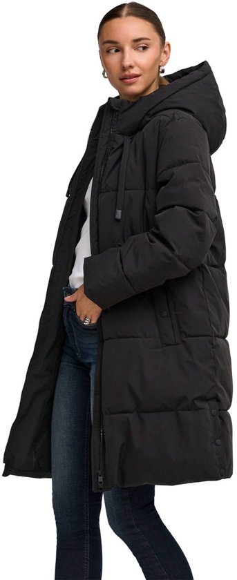 Vrouw in zwarte lange gewatteerde jas met capuchon, opzij gefotografeerd.