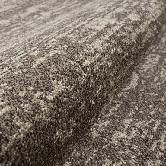 Bruin vloerkleed met een abstract patroon in bruin en beige tinten. De textuur is dicht en pluizig.