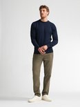 Model in marineblauwe trui en olijfgroene corduroy broek, staand tegen een witte achtergrond.