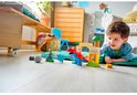 Een jongetje speelt met LEGO Duplo blokken, waaronder een rode en blauwe dinosaurus, groene goblin en een fort.