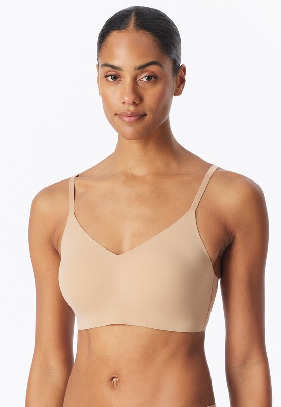 Model draagt een beige, naadloze bustier met V-hals en dunne bandjes.