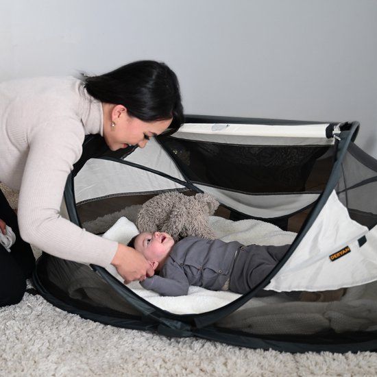 Moeder kijkt naar baby in Deryan Baby Luxe campingbedje, met teddybeer.