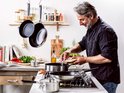 Man kookt op gasfornuis met KitchenAid pannen, snijdt ui.