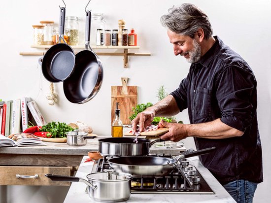 Man kookt op gasfornuis met KitchenAid pannen, snijdt ui.