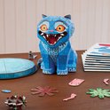 Blauwe, geometrische kat met rode ogen, op een tafel. Naast de kat liggen puzzelonderdelen en een stapel vellen.