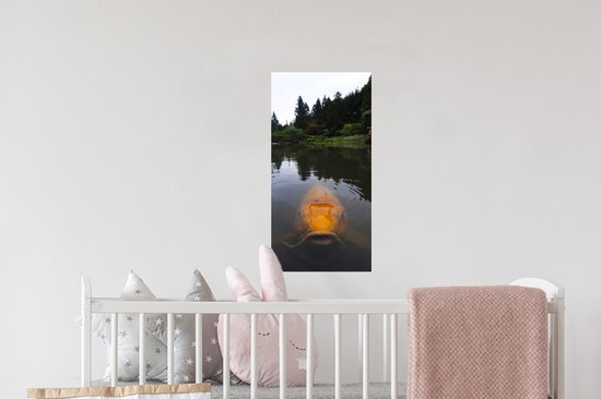 Une grande carpe koï orange nage dans un étang avec des arbres en arrière-plan.