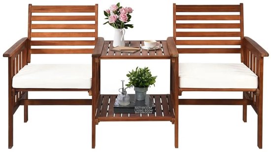 Een bruine houten tuinset met twee witte kussens en een centrale tafel met decoratie. De tafel heeft twee planken.