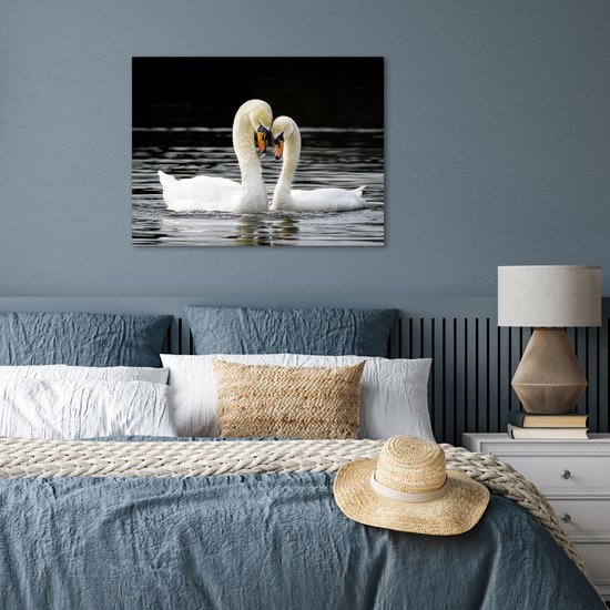 Deux cygnes blancs au bec orange nagent dans l'eau sombre, leurs cous forment un cœur, accrochés au mur dans une chambre.