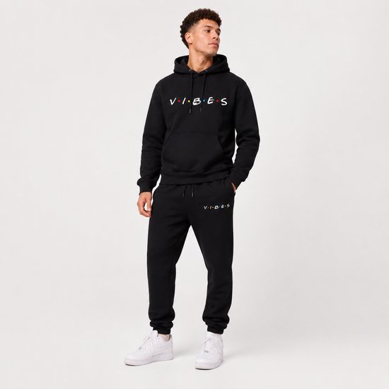 Man in een zwarte hoodie met 'VIBES' print en bijpassende joggingbroek.