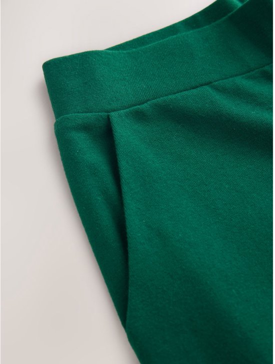 Detail van een groene wijde broek met steekzak en elastische tailleband.