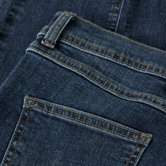Dichtbij detail van donkerblauwe spijkerbroek met oranje stiksels op de achterzakken en tailleband.