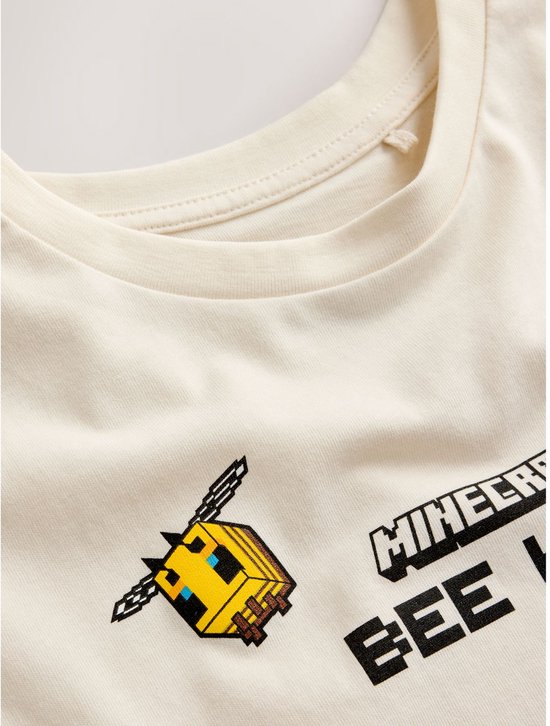 Detail van de Minecraft print op een crème T-shirt: een pixel bij en de tekst 'MINECRAFT BEE KIND'.