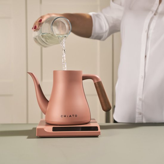 Roze waterkoker op roze basis, iemand giet water in de waterkoker.