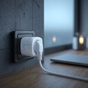 Een witte Wi-Fi slimme stekker is in een wandstopcontact gestoken, met een oplaadkabel die eraan is bevestigd. Een laptop staat op een houten tafel.