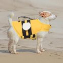 Witte hond met bruine vlekken, nat, op strand, draagt geel zwemvest met zwart gestreepte vleugels en witte cirkels.