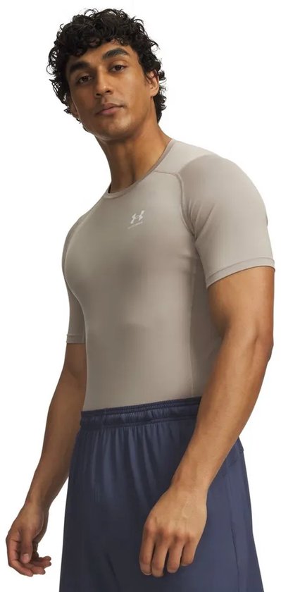 Man met krullend haar draagt een lichtbruin Under Armour Heatgear Armour compressie T-shirt met korte mouwen en een wit logo.