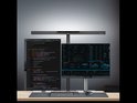 Zwarte bureaulamp verlicht twee computerdisplays met code en grafieken.