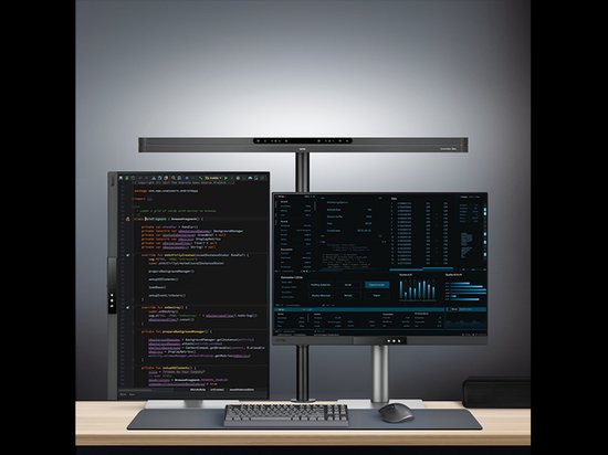 Zwarte bureaulamp verlicht twee computerdisplays met code en grafieken.