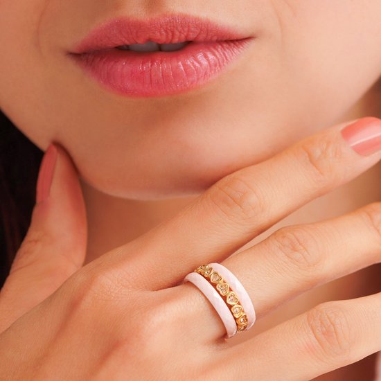Een dame draagt een gouden ring met hartvormige zirkonia's en een witte ring met gouden details.