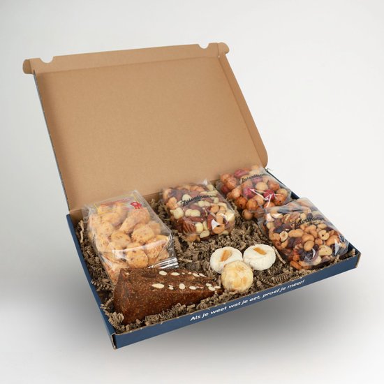 Un gâteau brun foncé et ferme avec des morceaux d'amandes, à côté de trois biscuits blancs ronds avec des abricots secs. Entouré de quatre sachets de noix mélangées et de snacks.