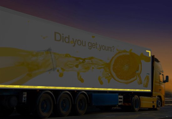 Gele vrachtwagen met de tekst "Did you get yours?", sinaasappel en frisdrank reclame, met reflecterende tape.
