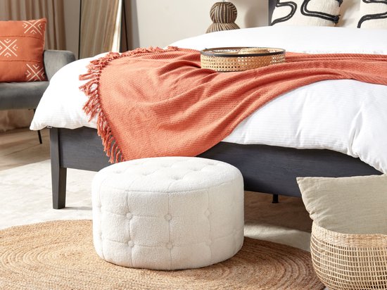 Witte bouclé poef met knopen, voor een bed in een slaapkamer.