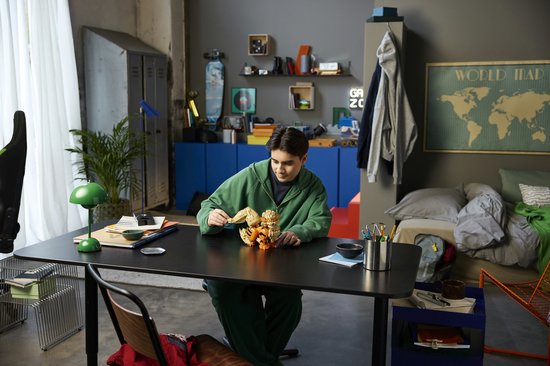 Jongeman in groene hoodie zit aan een bureau met een LEGO Arcanine figuur.