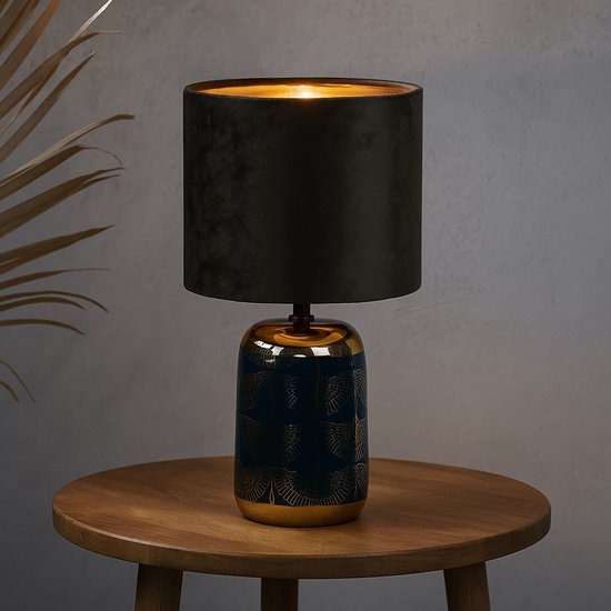 Tafellamp met blauwe voet met gouden bladmotief en zwarte fluwelen kap, op een houten bijzettafel.