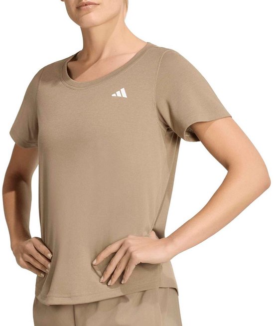 Een vrouw poseert in een beige Adidas sportshirt met ronde hals en korte mouwen, met het Adidas logo op de borst.