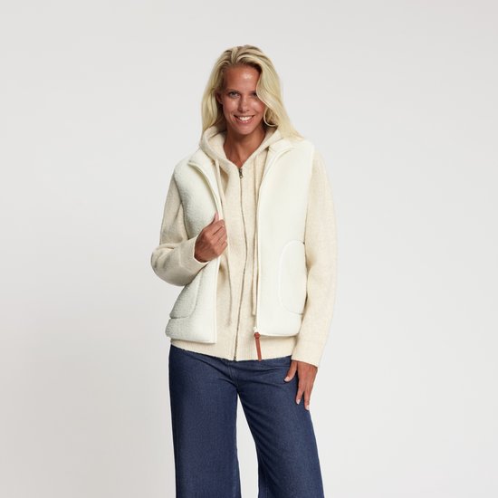 Model draagt een gebroken wit teddy bodywarmer over een bijpassende hoodie en donkerblauwe jeans.